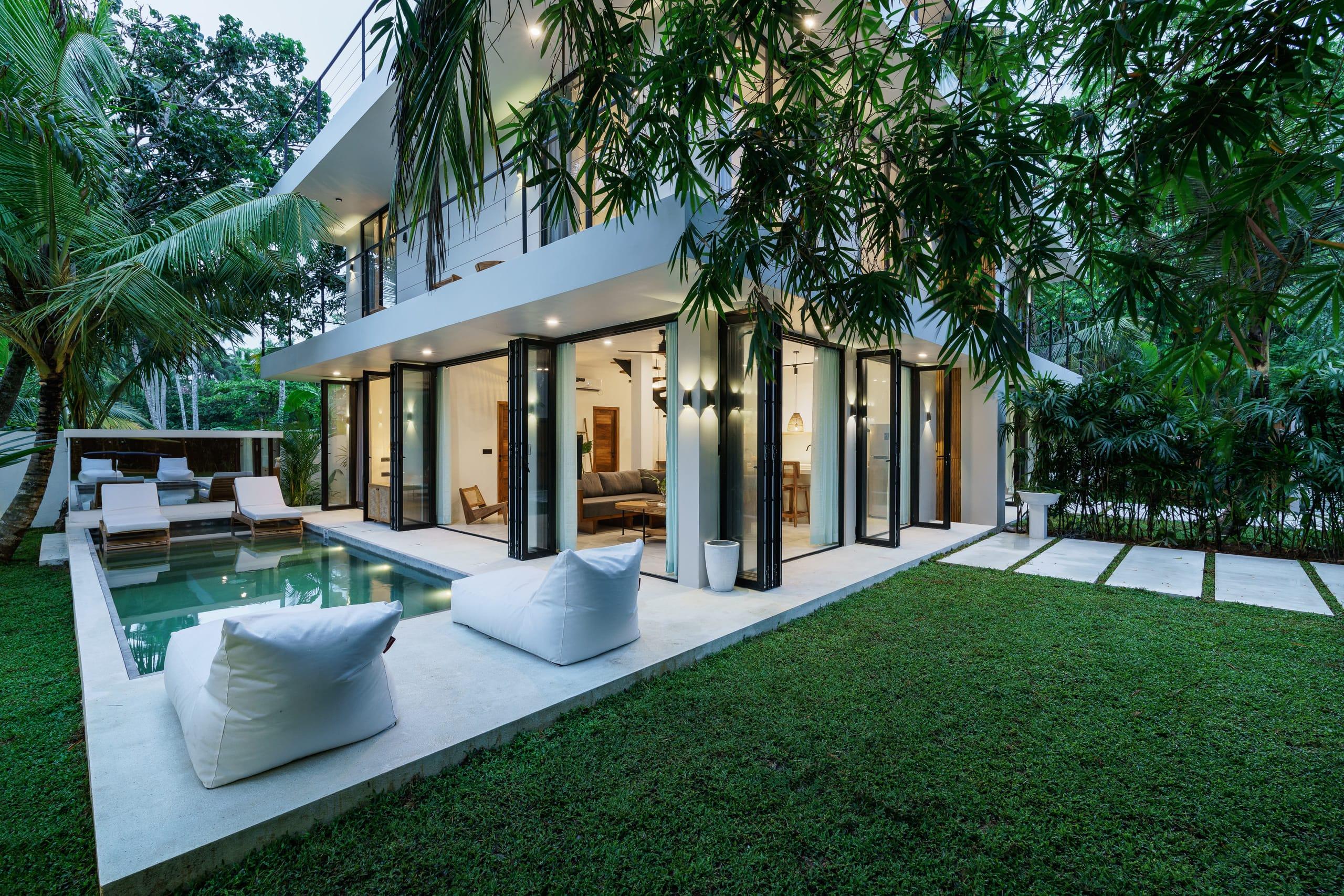 A Terra villa at dusk - the lit living room, plunge pool and bean bags under the palms
