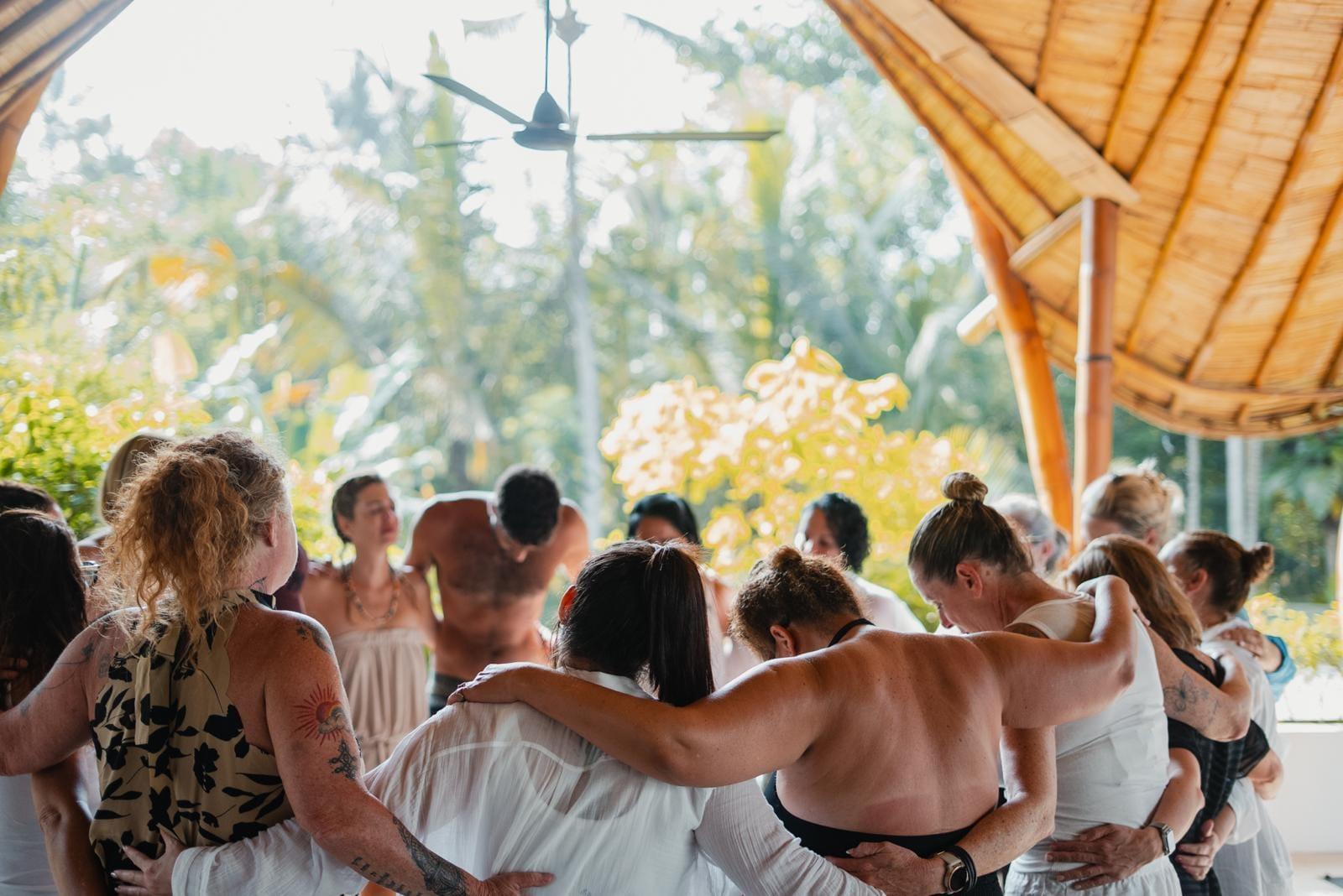 The group closing the week in a circle under the shala roof, arms around each other